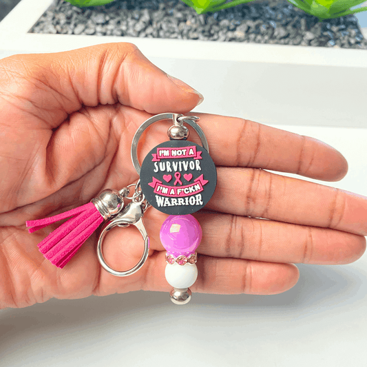 Keychain with pink tassel and text held in a hand against a neutral background