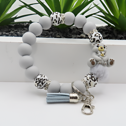 Bracelet with gray beads, animal print charms, and a tassel on a white surface with green plants in the background.