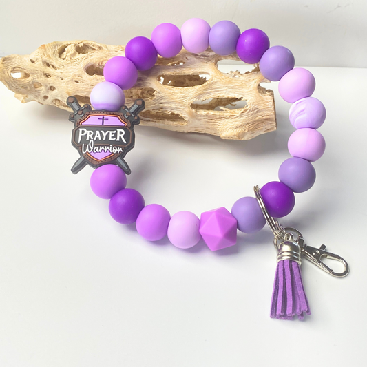 Purple beaded bracelet with a 'Prayer Warrior' charm on a white background