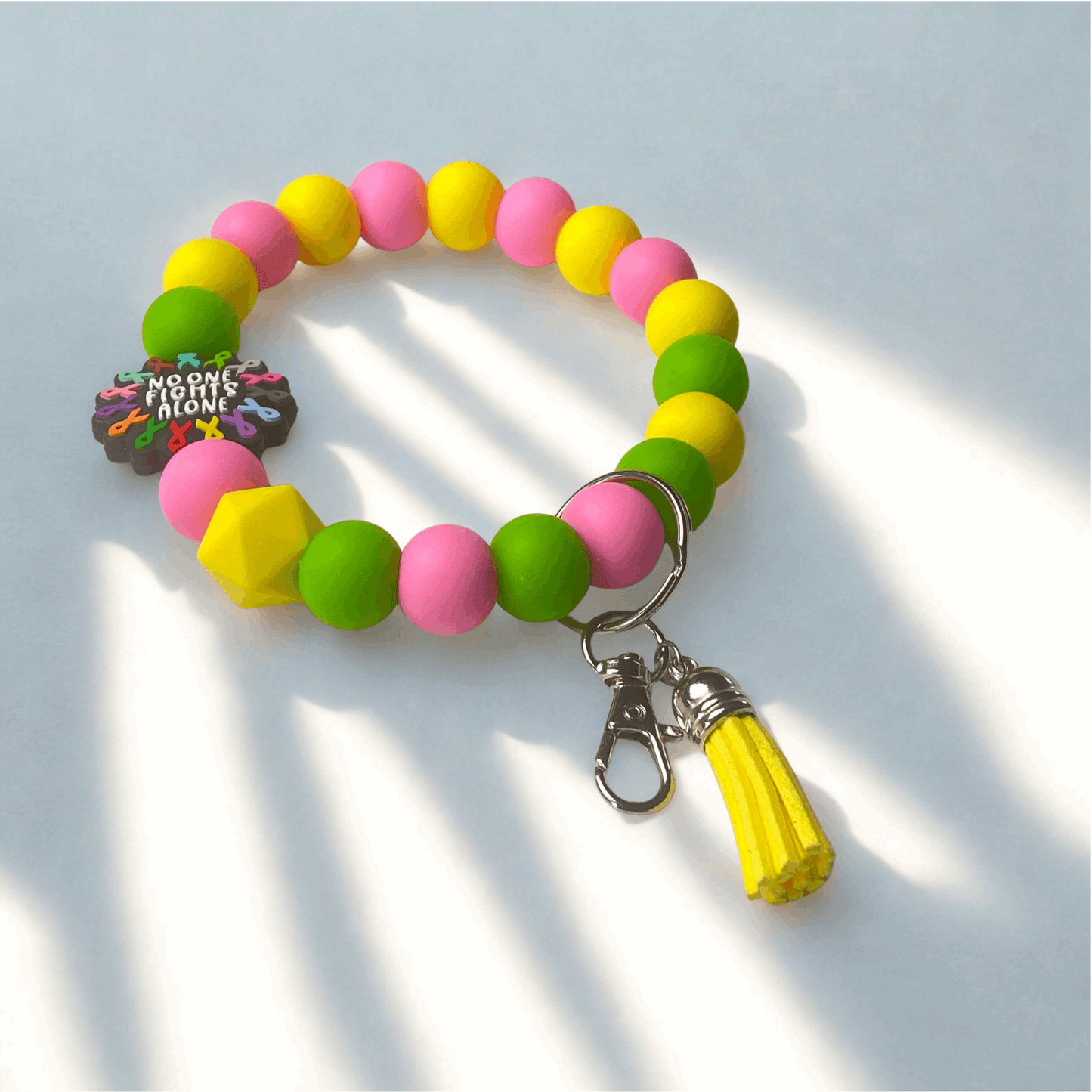 Colorful beaded bracelet with a yellow tassel charm on a light blue background