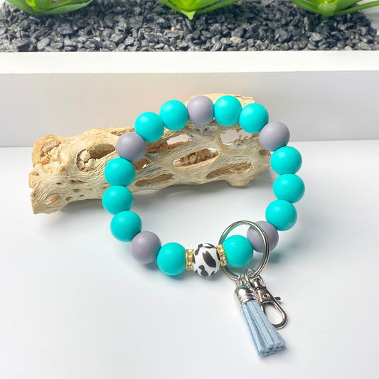 Turquoise and gray beaded keychain with a tassel on a white surface.