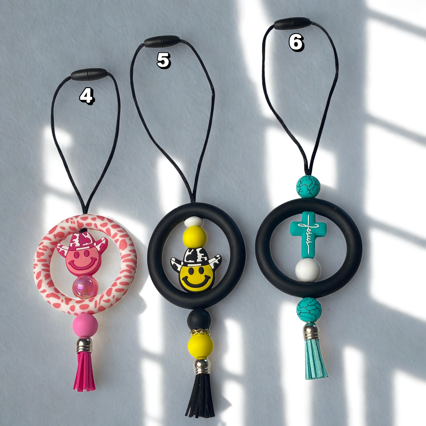 Three decorative keychains with colorful beads and tassels on a light gray background.