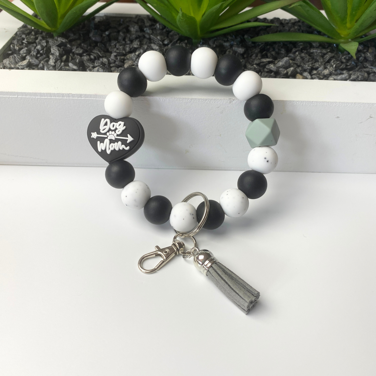 Beaded bracelet with a tag and tassel charm on a white surface with plants in the background