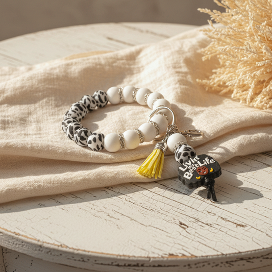 Bracelet with white beads, leopard print accents, and a keychain with a yellow tassel on a light surface.