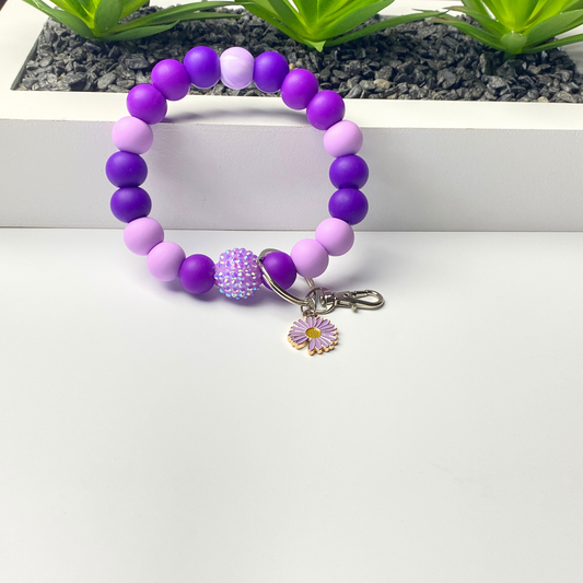 Purple and pink beaded bracelet with a keychain on a white surface