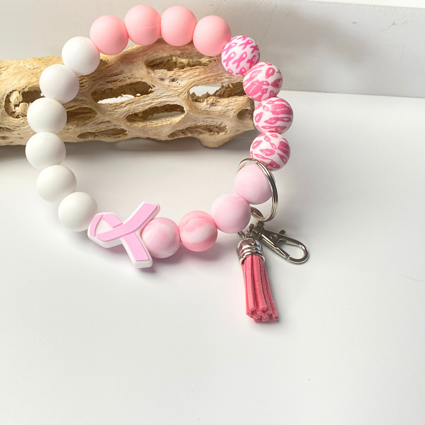 Pink and white beaded bracelet with a keychain and tassel on a light background