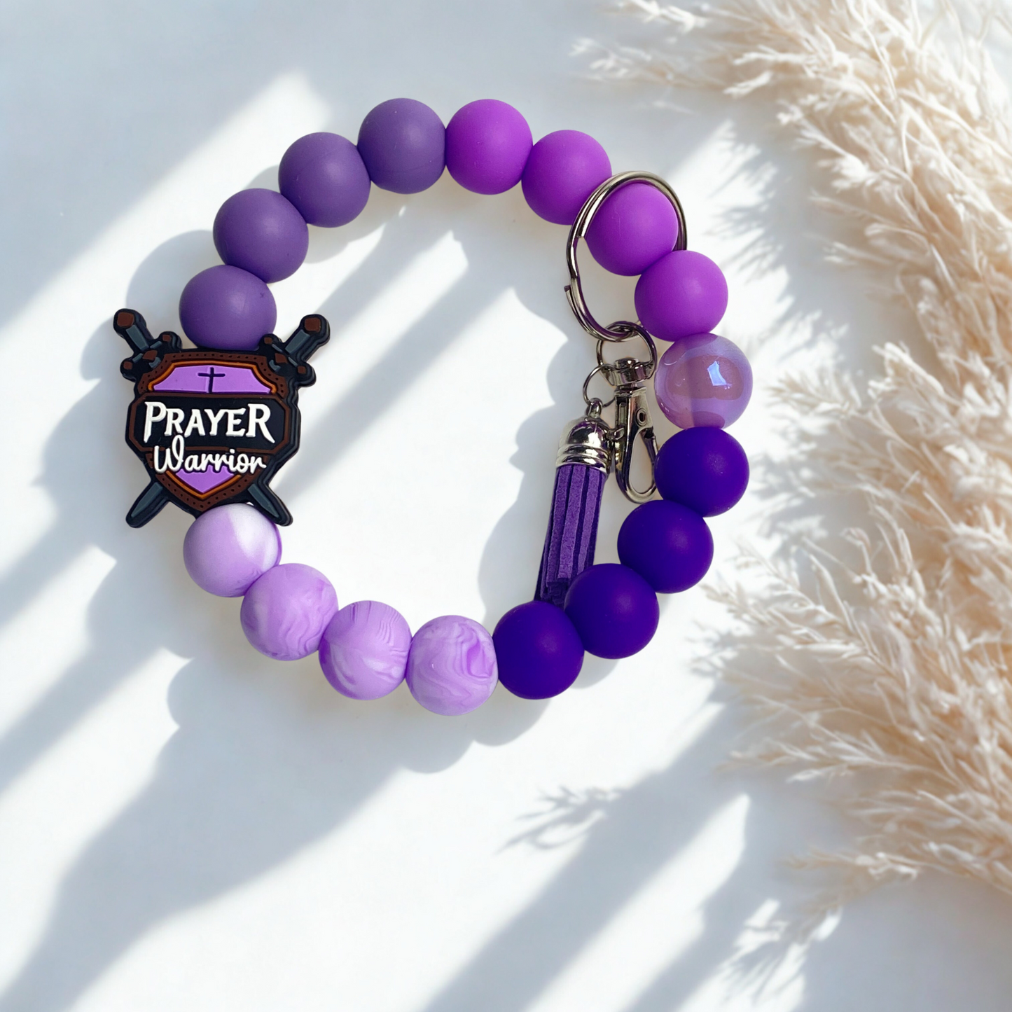 Purple beaded bracelet with a 'Prayer Warrior' charm on a light background