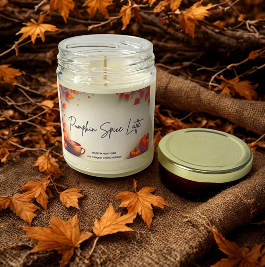 Pumpkin spice latte candle in a jar with a label on a burlap surface with autumn leaves.
