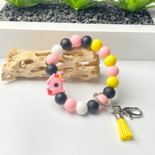 Colorful beaded keychain with a pink birdhouse charm on a white surface.
