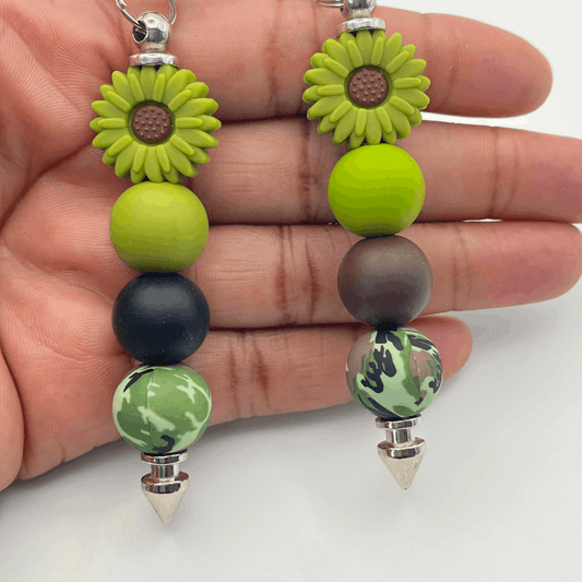 Hand holding a beaded keychain with green and brown beads and sunflower designs.