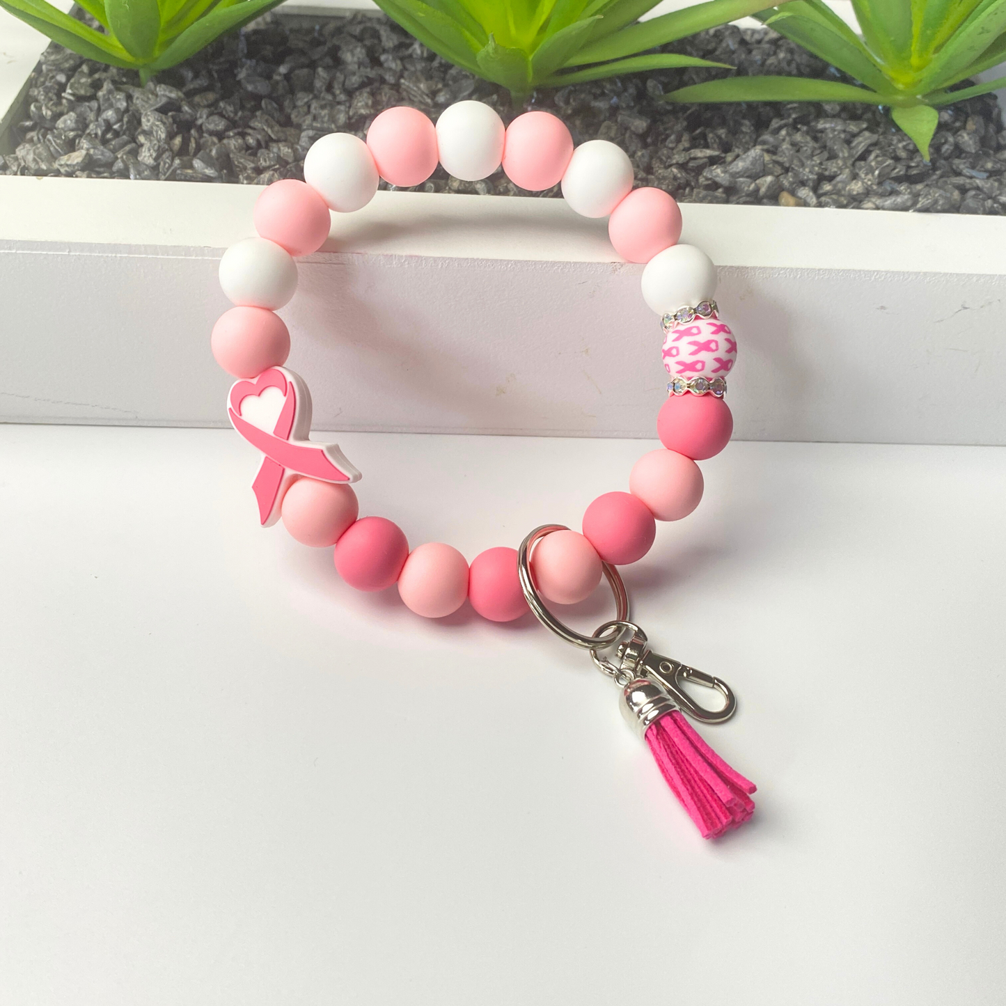 Pink and white beaded bracelet with a keychain and tassel on a white surface.