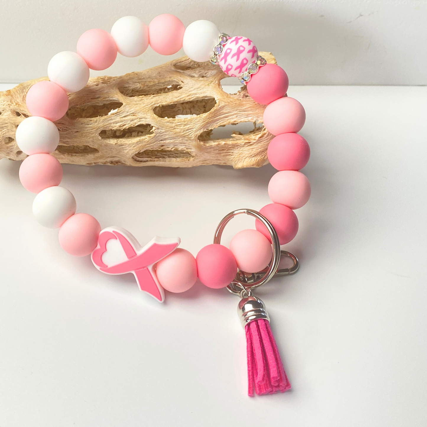 Pink and white beaded bracelet with a pink ribbon charm and tassel on a light background