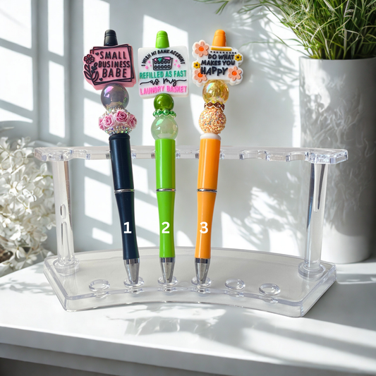 Three decorative pens on a clear stand with colorful accents and text, set against a bright background.