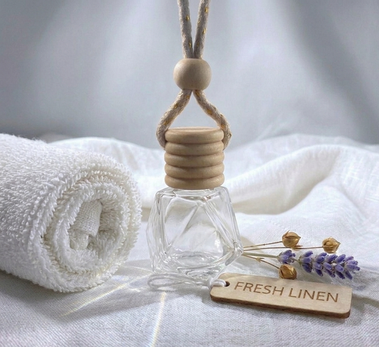 Glass diffuser with wooden cap on a white fabric background, featuring a 'Fresh Linen' tag.