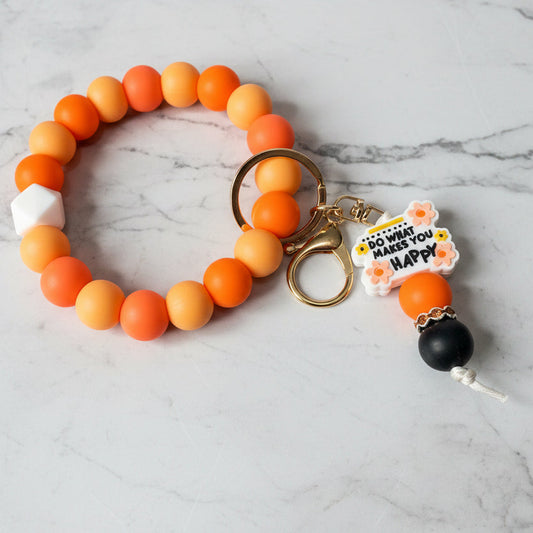 Orange beaded keychain with a black charm on a marble surface
