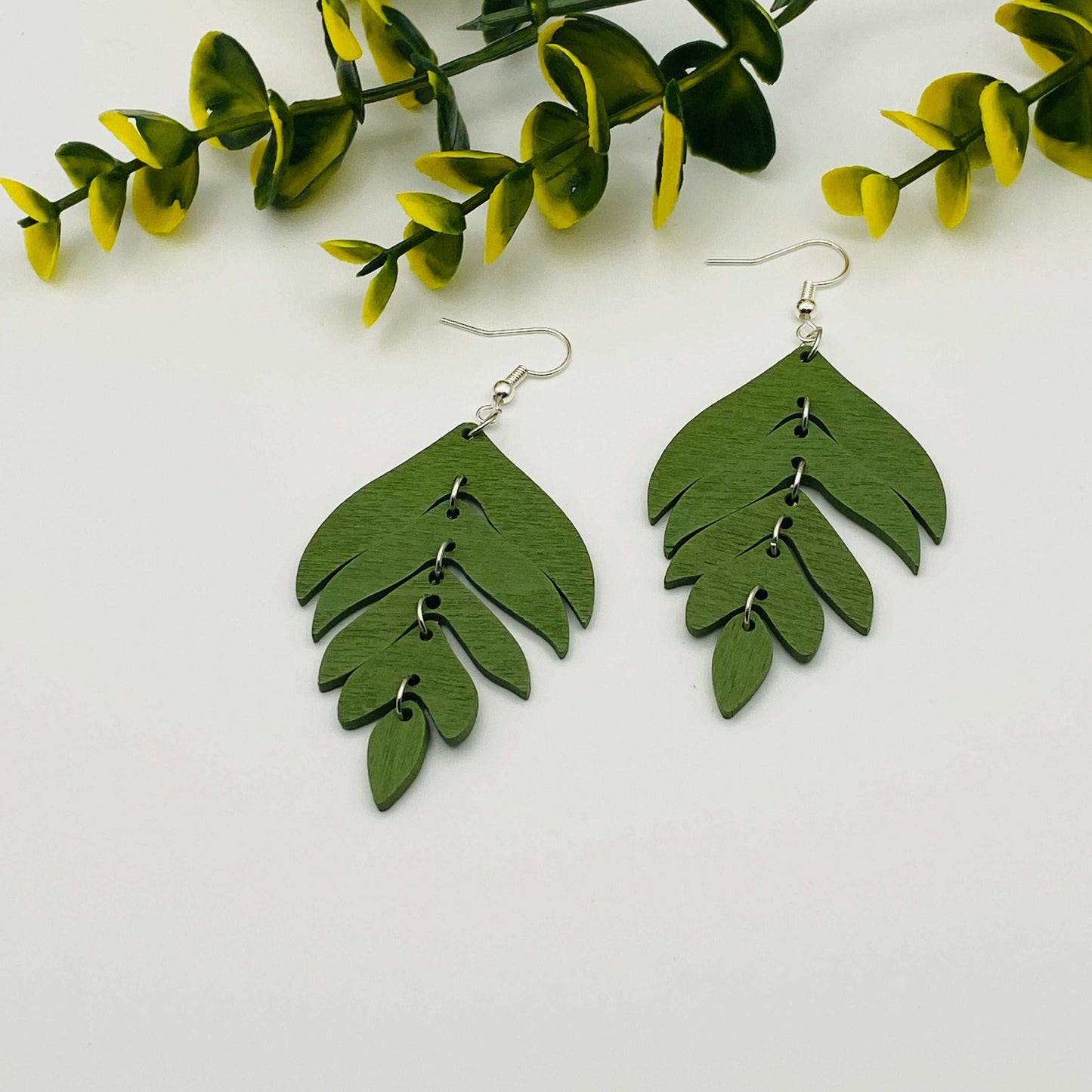 Green leaf-shaped earrings on a white background with green leaves.