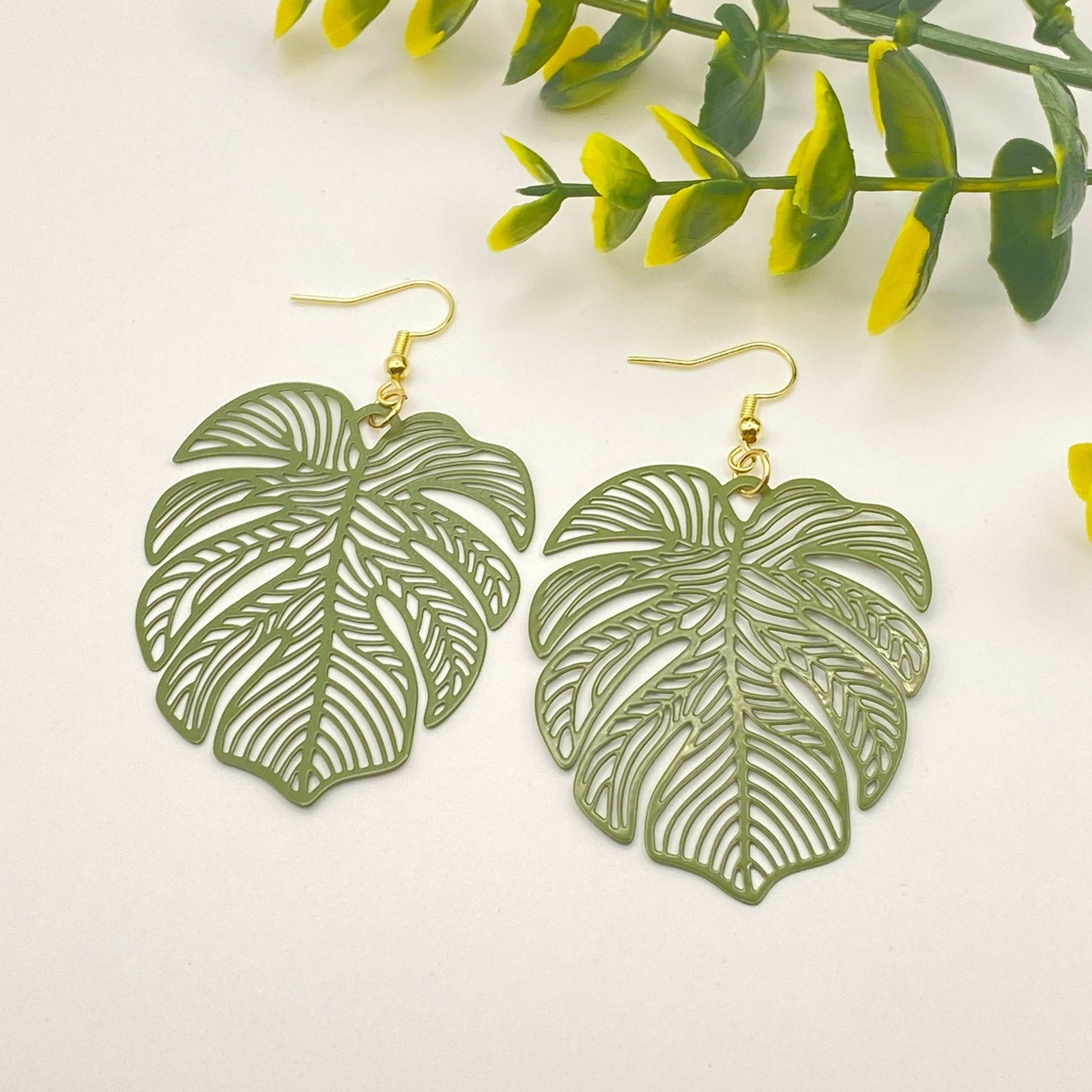 Leaf-shaped earrings on a white background with green leaves.