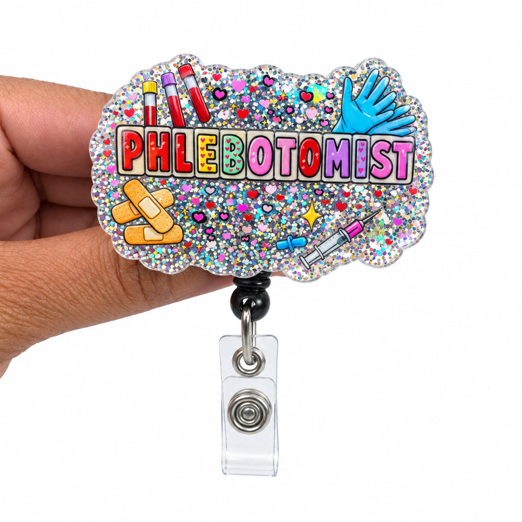 A hand holding a custom glittery acrylic badge reel featuring the text 'PHLEBOTOMIST' in pink letters, surrounded by colorful medical and cosmetic illustrations, on a plain white background.
