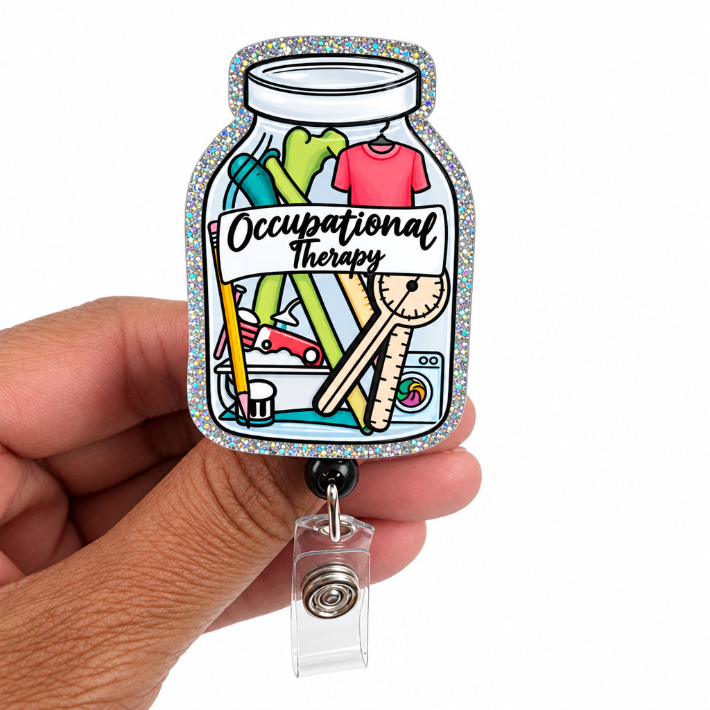 A hand holds a glittery silver badge reel featuring a colorful illustration of an occupational therapy jar with the words 'Occupational Therapy' on a white background.