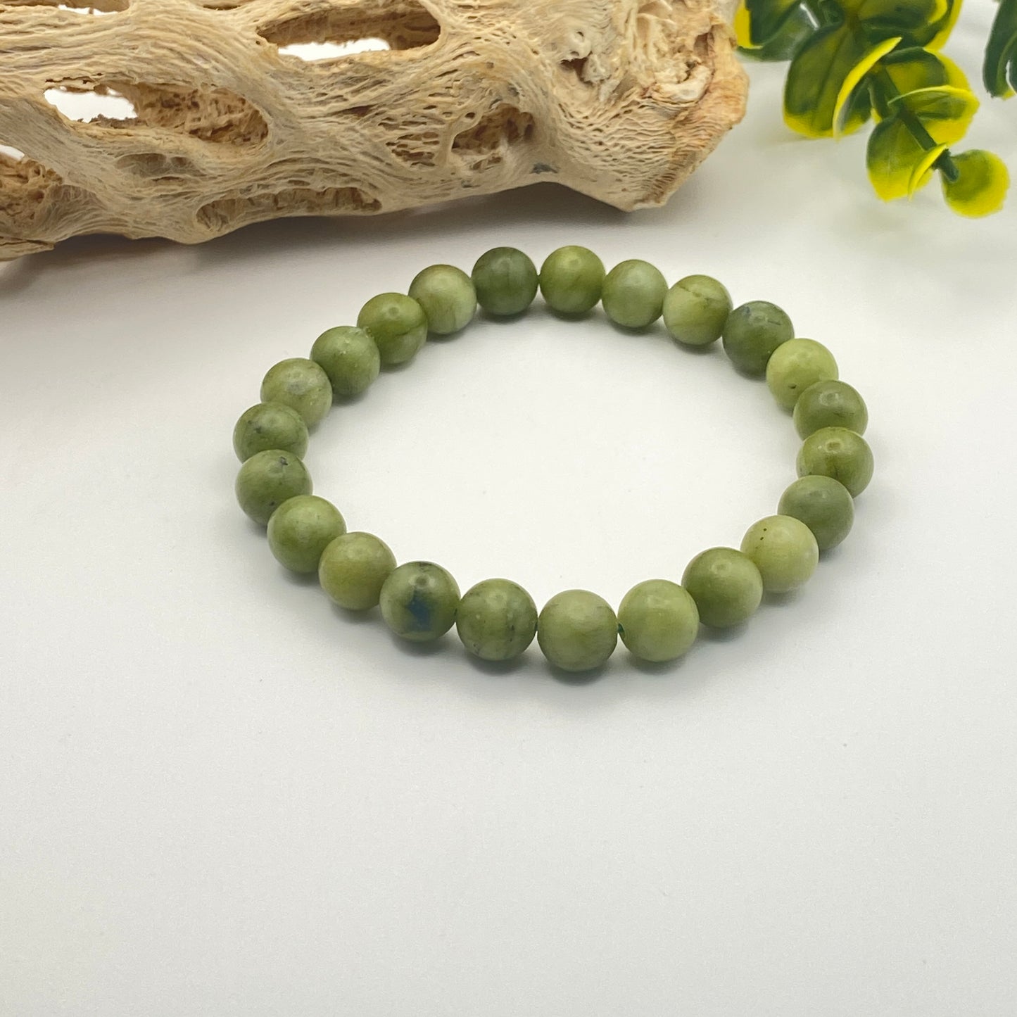 Green beaded bracelet on a white surface with natural wood and green leaves in the background