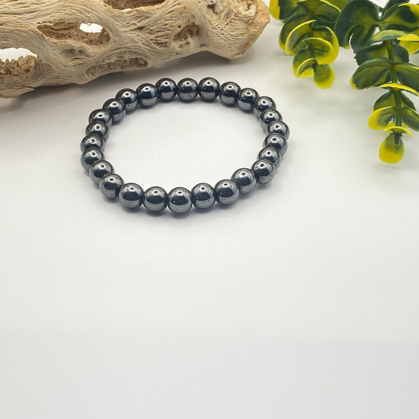 Black beaded bracelet on a white surface with natural elements in the background