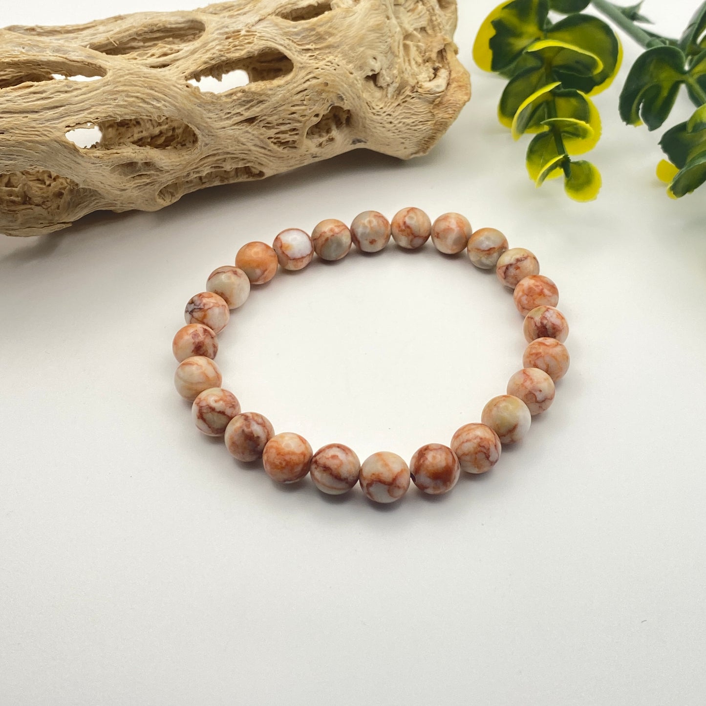 Beaded bracelet on a white surface with natural elements in the background