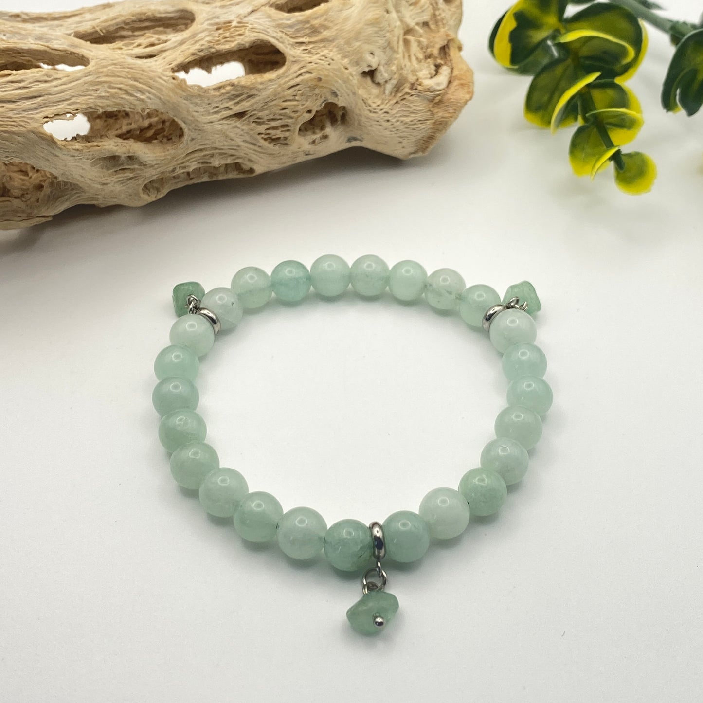 Green beaded bracelet on a white surface with natural elements in the background
