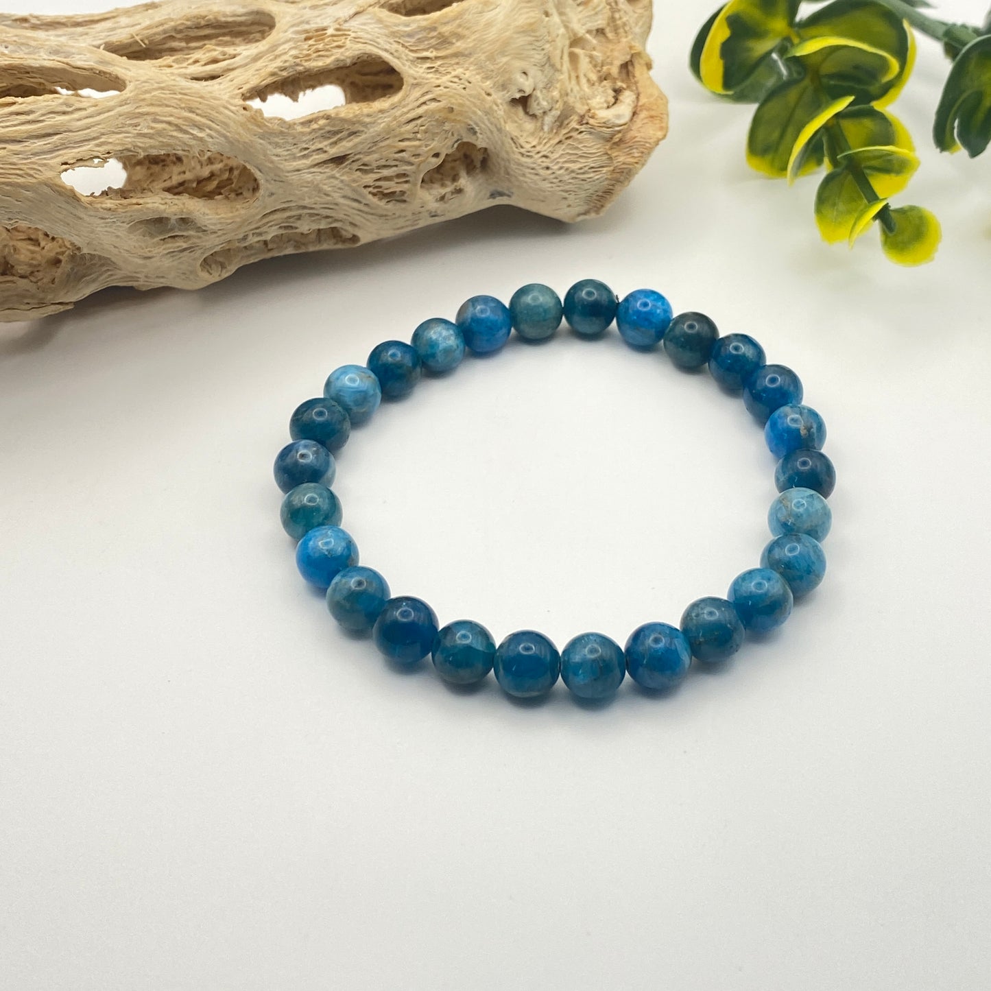 Blue beaded bracelet on a white surface with natural elements in the background