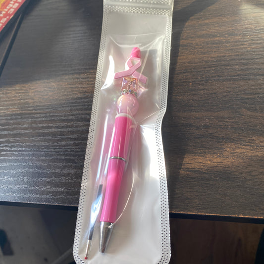 Pink pen with a breast cancer awareness ribbon in clear packaging on a wooden surface