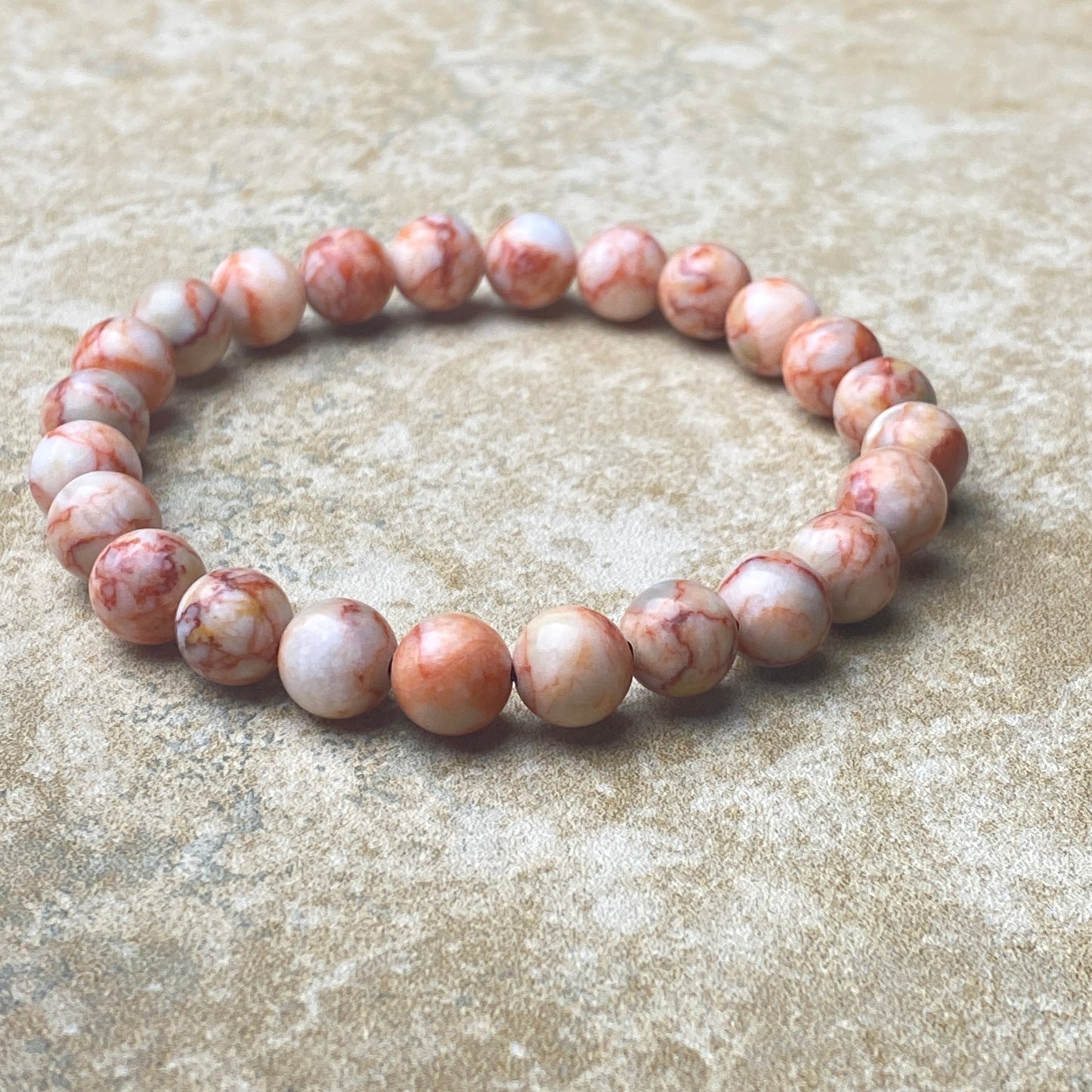 Beaded bracelet with pink and white marbled beads on a textured beige surface