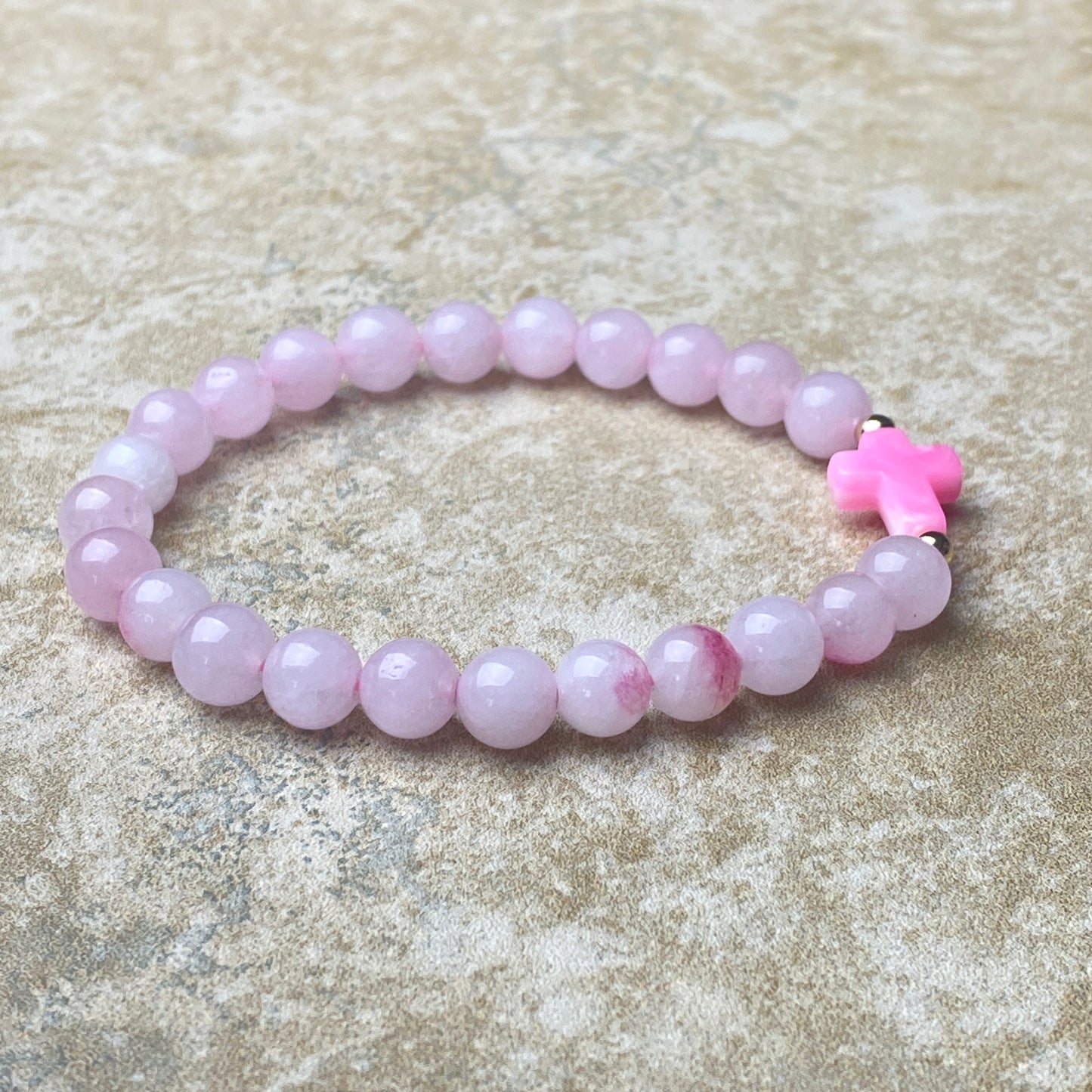 Pink beaded bracelet with a cross charm on a textured surface