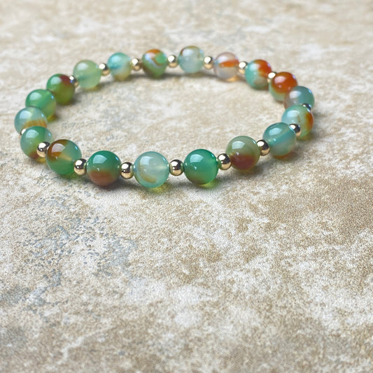 Beaded bracelet with green and gold beads on a textured surface