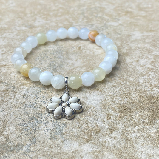 Beaded bracelet with a silver flower charm on a textured surface