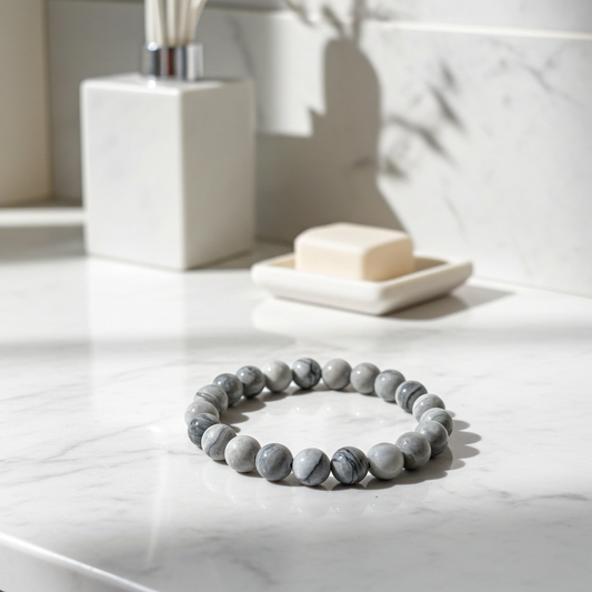 Gray beaded bracelet on a marble surface with a soap dish and bar of soap in the background.