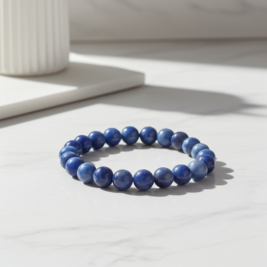 Blue beaded bracelet on a light surface with a white candle in the background