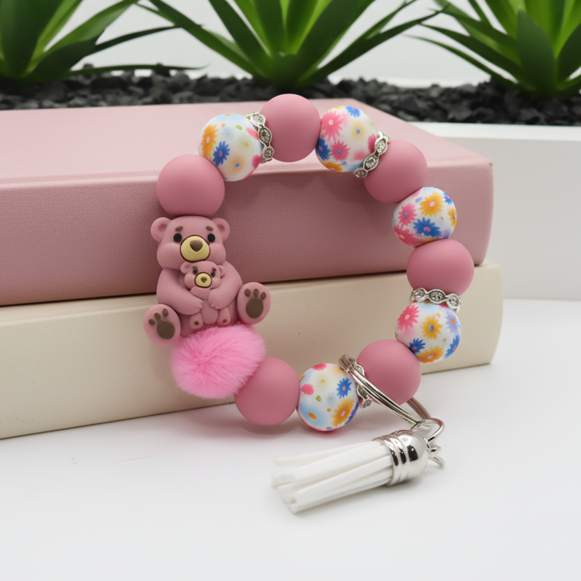 Pink beaded bracelet with a teddy bear charm on a white surface with plants in the background