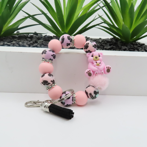 Bracelet with pink beads and a teddy bear charm on a white surface with plants in the background