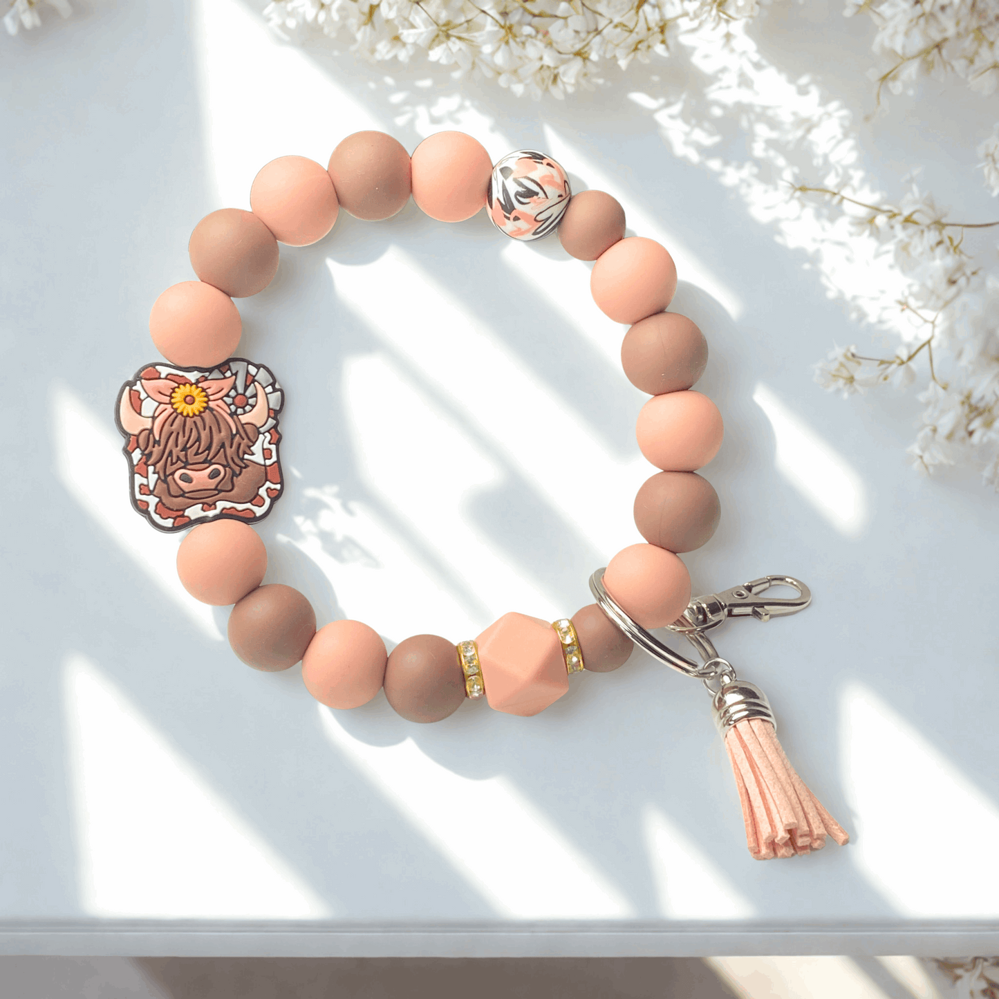 Beaded bracelet with a tassel on a white surface with flowers in the background