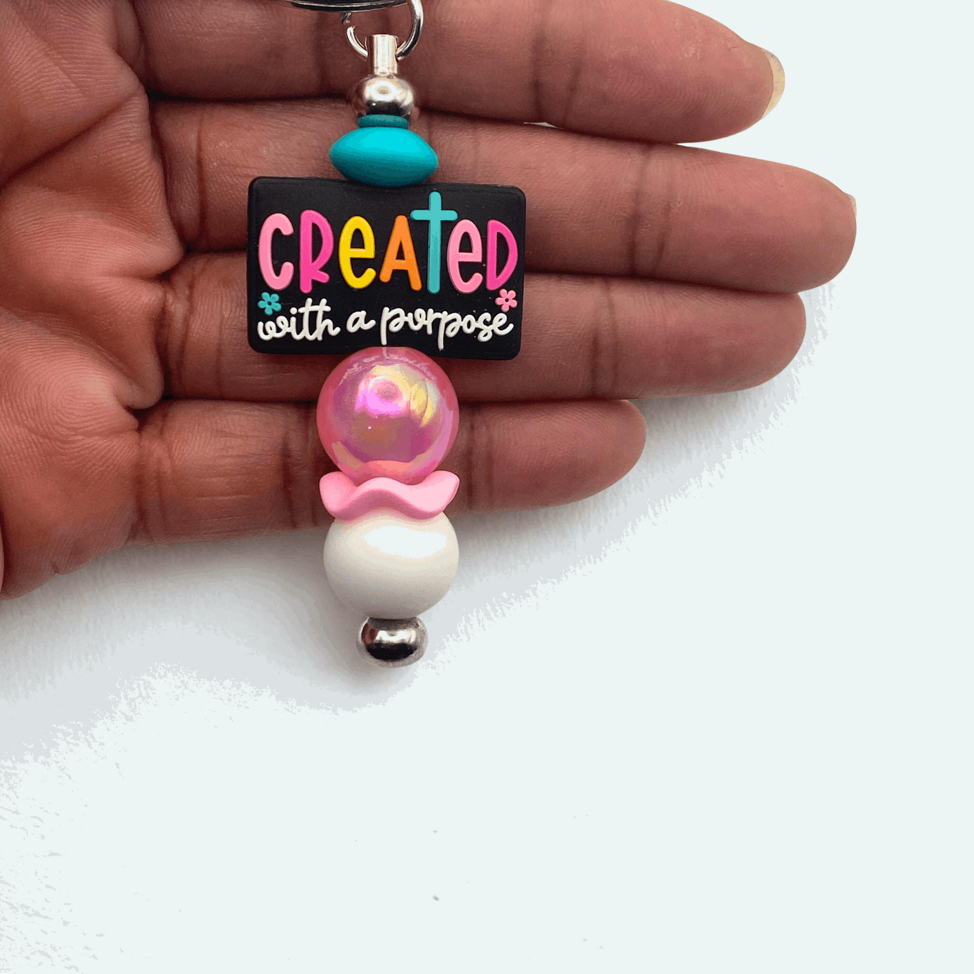 Colorful keychain with 'Created with a Purpose' message held in a hand on a white background
