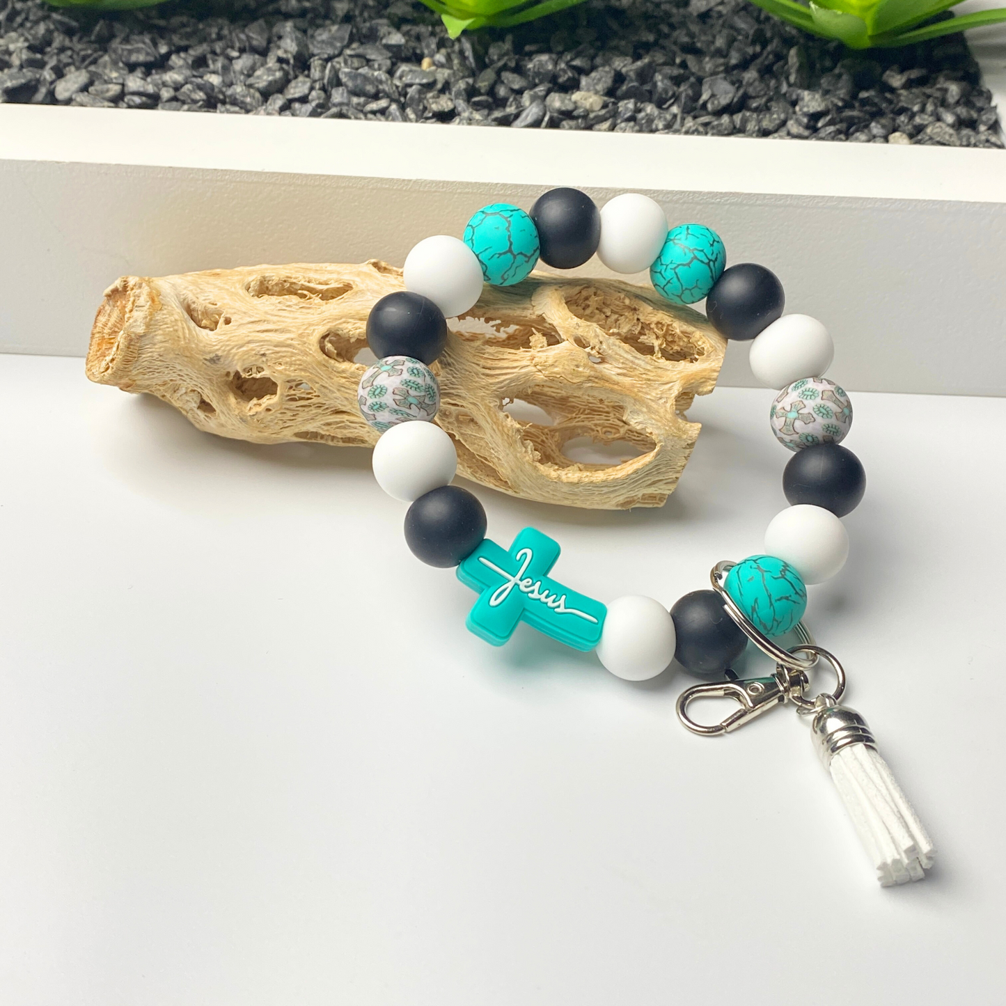 Beaded bracelet with turquoise cross charm and white, black, and blue beads on a white surface.