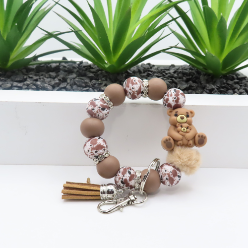 Bracelet with bear charm and tassel on a white surface with green plants in the background