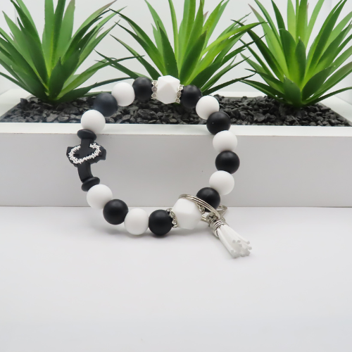 Black and white beaded bracelet with key charm on a white surface with plants in the background