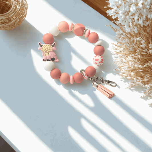 Pink and white beaded bracelet with a cow charm on a light surface.