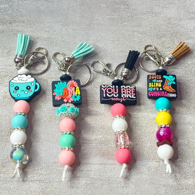 Five colorful keychains with beads and tassels on a gray surface