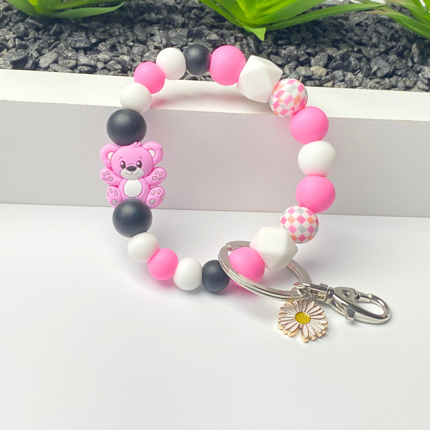 Bracelet with pink, black, and white beads and a teddy bear charm on a white background.
