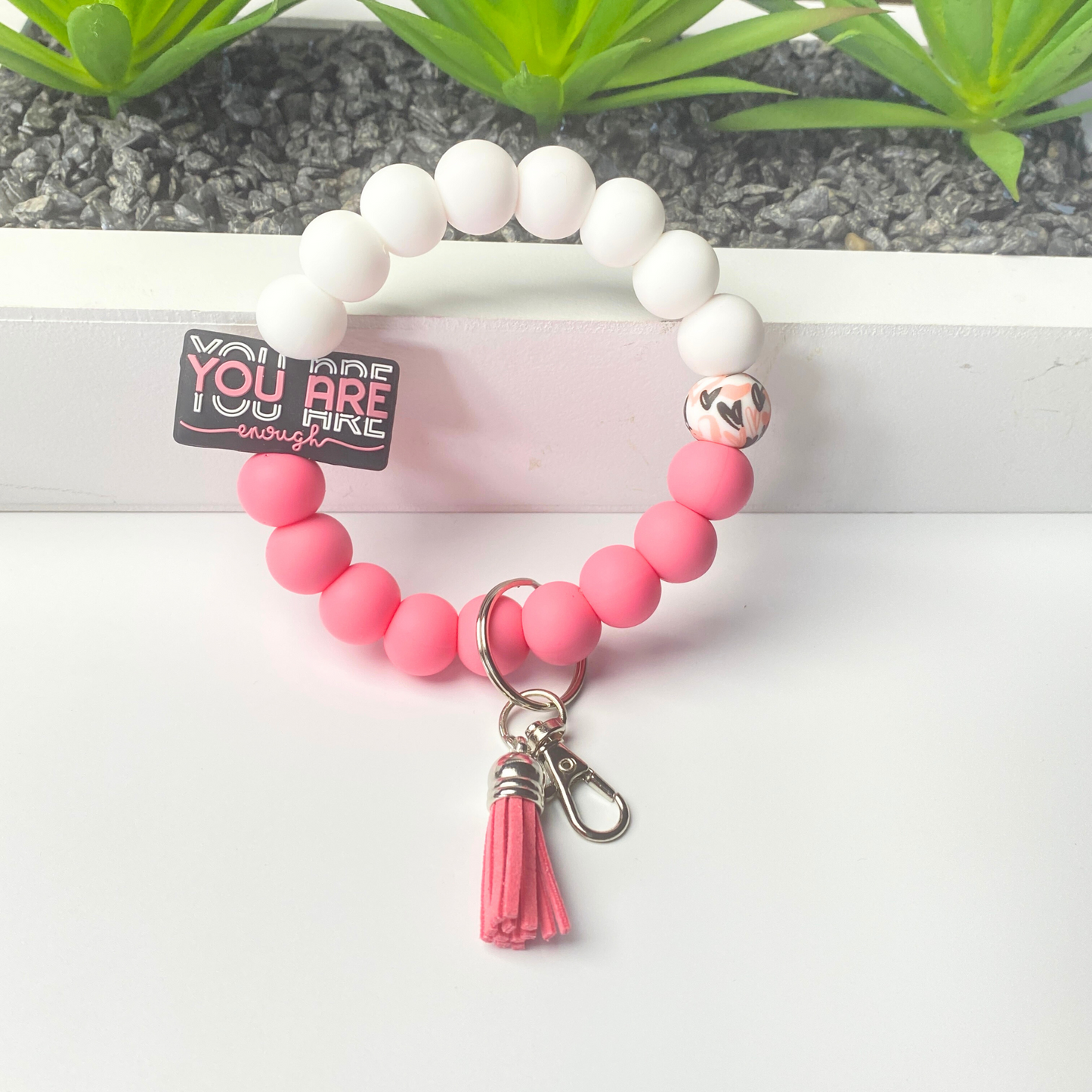 Pink beaded keychain with tassel on a white surface