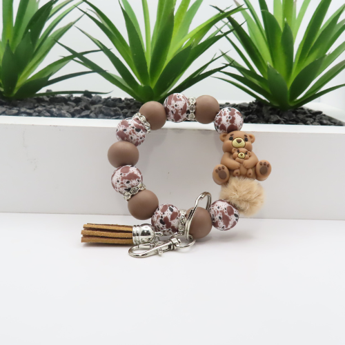 Bracelet with teddy bear charm and keychain on a white surface with plants in the background