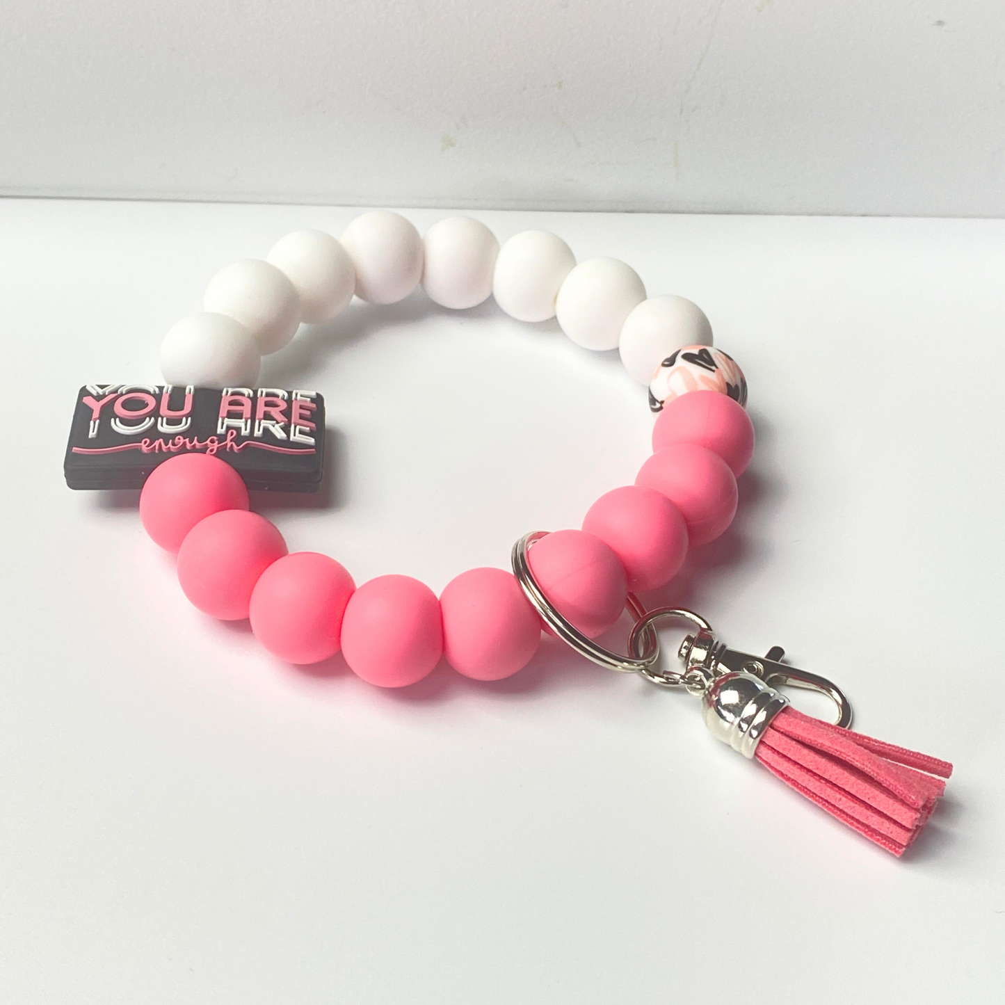 Pink and white beaded bracelet with a tassel charm on a white background