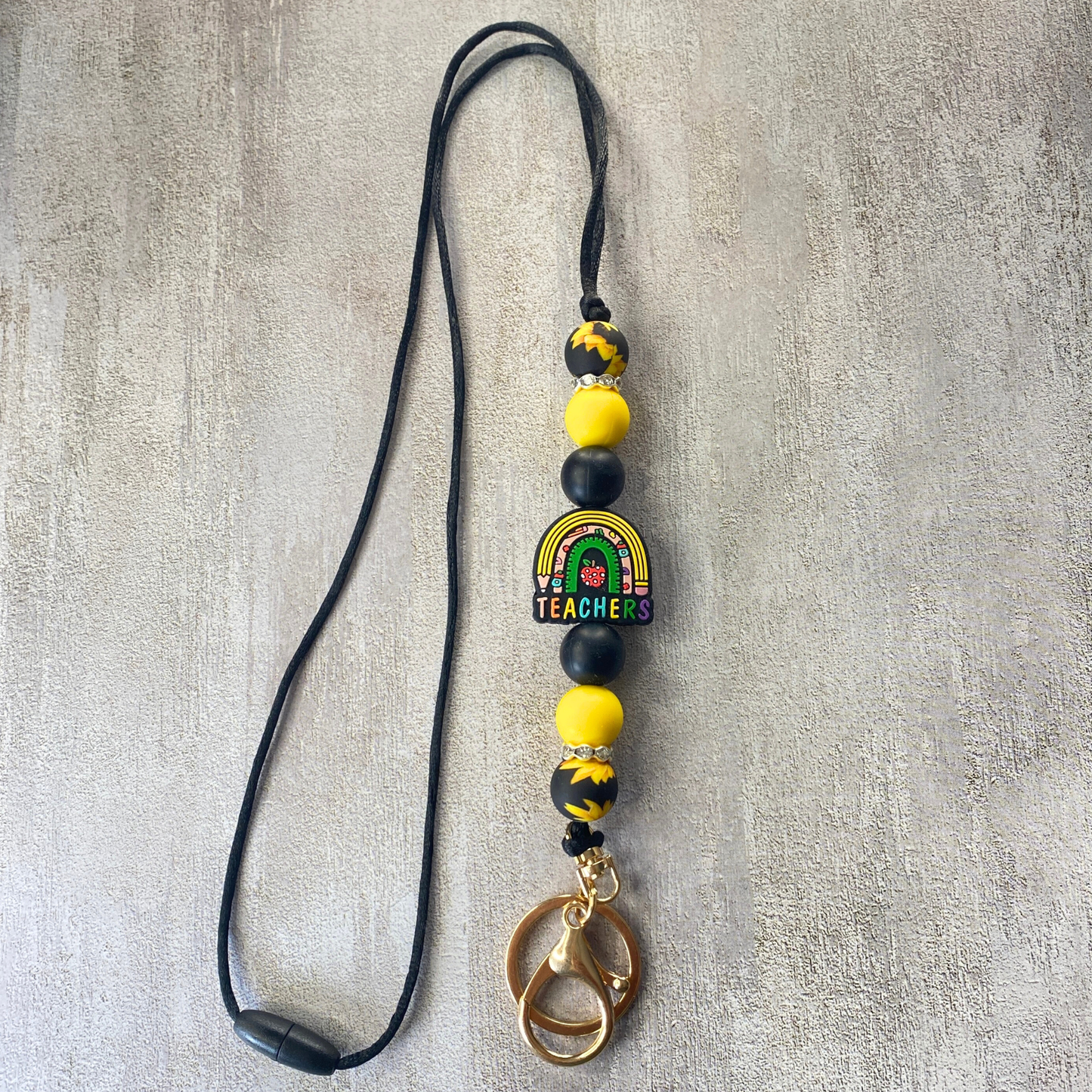 Beaded keychain with rainbow design and 'Teachers' text on a textured surface