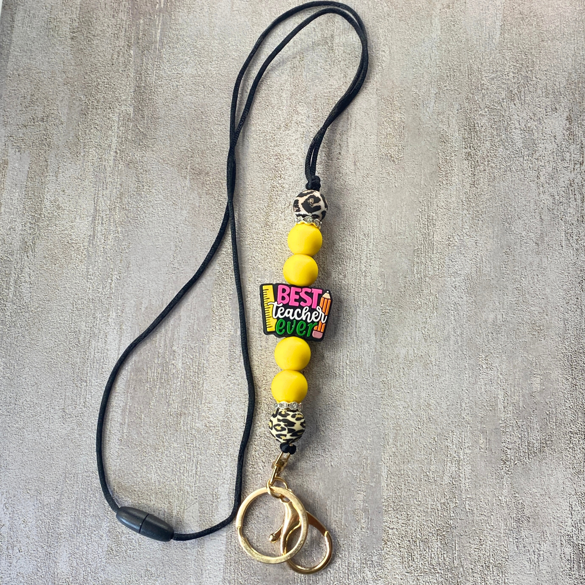 Lanyard with yellow beads and 'Best Teacher Ever' charm on a gray background